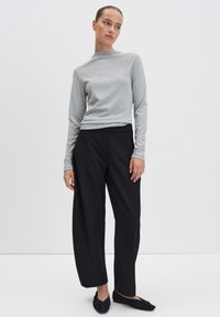 Maglietta grigia a maniche lunghe, pantaloni neri a gamba larga e scarpe flat nere. Tessuto liscio con una vestibilità rilassata e dettagli sottili nel colletto della maglietta.