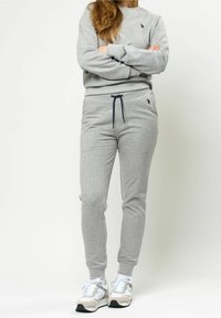 Grå fleecetröja med lång ärm och rund halsringning, kombinerad med matchande sweatpants med marinblå dragsko, komplett med vita sneakers.