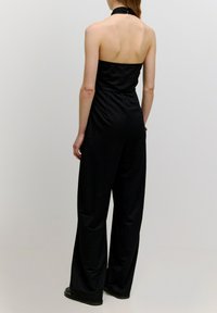 Schwarzer trägerloser Jumpsuit mit Halterneck, weitem Bein Design, glatter Stofftextur und minimalistischem Schnitt.