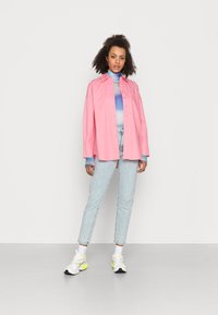 Camisa rosa de botões com um corte descontraído, combinada com um pulôver de gola alta em azul degradê, jeans de ganga clara e ténis coloridos.
