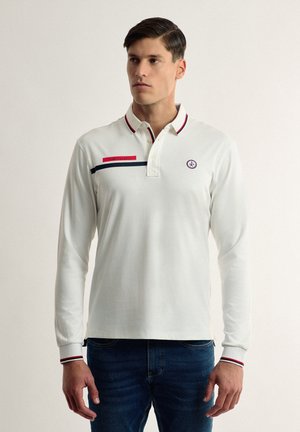 Camisa polo blanca de manga larga con collar, con rayas rojas y azul marino, y un logo bordado en el lado izquierdo del pecho. Puños con rayas delgadas.