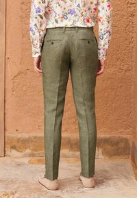 Zielone lniane spodnie o wąskim kroju, z tylnią kieszenią zapinaną na guzik. Połączone z jasnobeżowymi mokasynami.