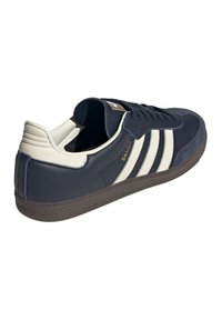 Sneaker Adidas Samba di colore blu navy con strisce bianche, linguetta del tallone beige, suola nera e "SAMBA" in lettere dorate sul lato.