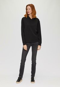 Sudadera con capucha negra de ajuste relajado, mangas largas y cordones ajustables. Combinada con jeans ajustados gris oscuro y zapatillas negras.