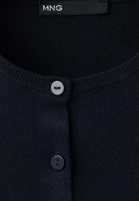 Gros plan d'un cardigan en maille bleu marine foncé avec deux boutons et une étiquette de marque MNG visible à l'encolure.
