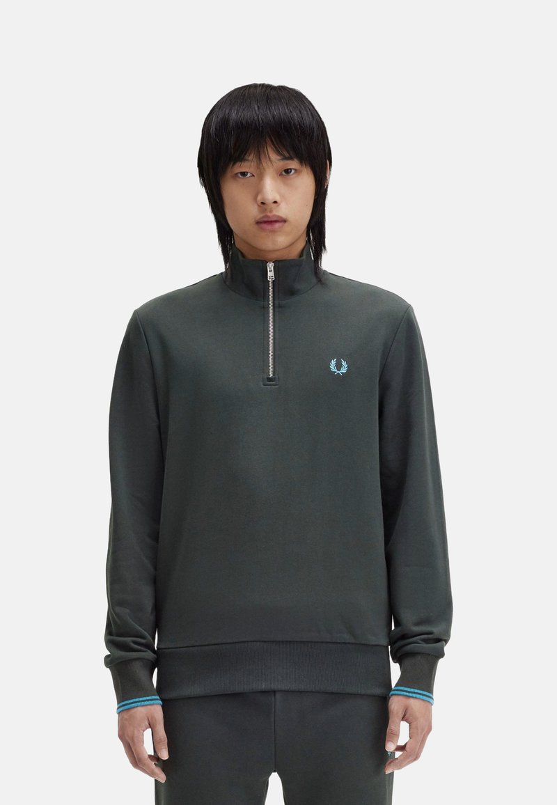 Sudadera de cuello alto de color verde oscuro con una textura suave, que presenta un pequeño logo azul y acentos azules contrastantes en los puños.