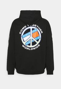 Sudadera negra con capucha que presenta un gran gráfico de símbolo de paz multicolor con el texto "UNÁMONOS EN TODO EL MUNDO" y "TOMMY JEANS" en blanco.