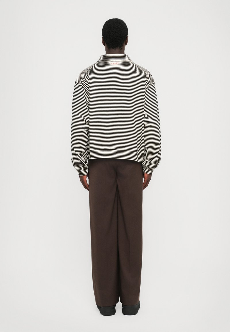 Gestreepte lange mouwen shirt in zwart en wit, met een kraag, gedragen met bruine wijde broek. Gladde textuur, relaxte pasvorm, minimale detailing.