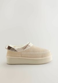 Beige instap schoen met een suède bovenwerk, zachte voering en contrasterende stiksels. Voorzien van een dikke, beige plateauzool en een patroonaccent op de hak.