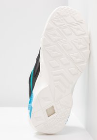 Semelle blanche texturée d'une chaussure de sport Reebok noire et bleue, montrant le motif de la bande de roulement et la fenêtre de rembourrage hexlite.