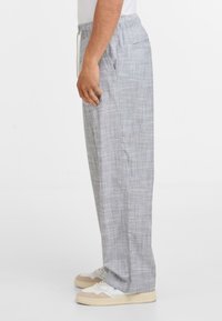 Světlé šedé, kostkované kalhoty na stažení vyrobené z měkké tkaniny. Mají boční kapsy a volný střih s rovným designem nohavic.