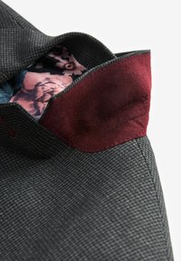 Grå tekstureret stof med en dyb rød accent ved kraven. Indvendigt har det et blomstermønster i nuancer af pink og blå.