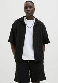 Black textured short-sleeve shirt with a wave pattern, paired with matching black shorts, and a white T-shirt underneath. Silver chain accessory.