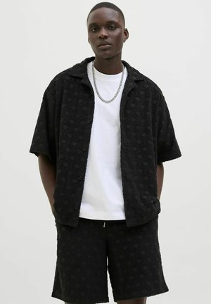Chemise noire à manches courtes avec un motif en vagues, assortie à un short noir, et un T-shirt blanc en dessous. Accessoire en chaîne en argent.