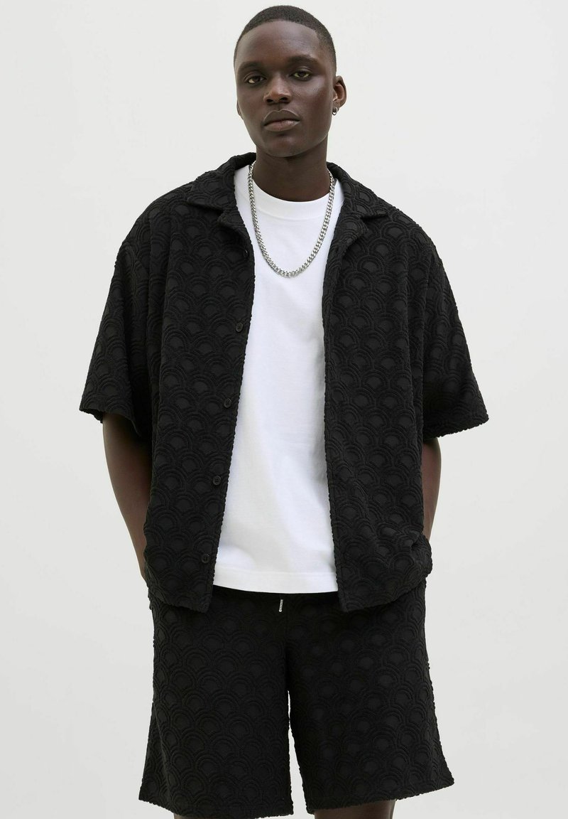 Black textured short-sleeve shirt with a wave pattern, paired with matching black shorts, and a white T-shirt underneath. Silver chain accessory.