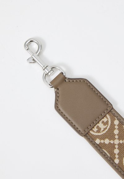 Fermeture en métal argenté attachée à une sangle en cuir marron et en tissu à motifs sur un fond blanc.