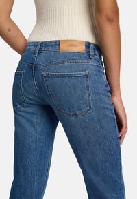 Jeans in denim blu con una lavatura media, dotati di un'etichetta in pelle con marchio nella parte posteriore della vita, due tasche posteriori e una gamba dritta.
