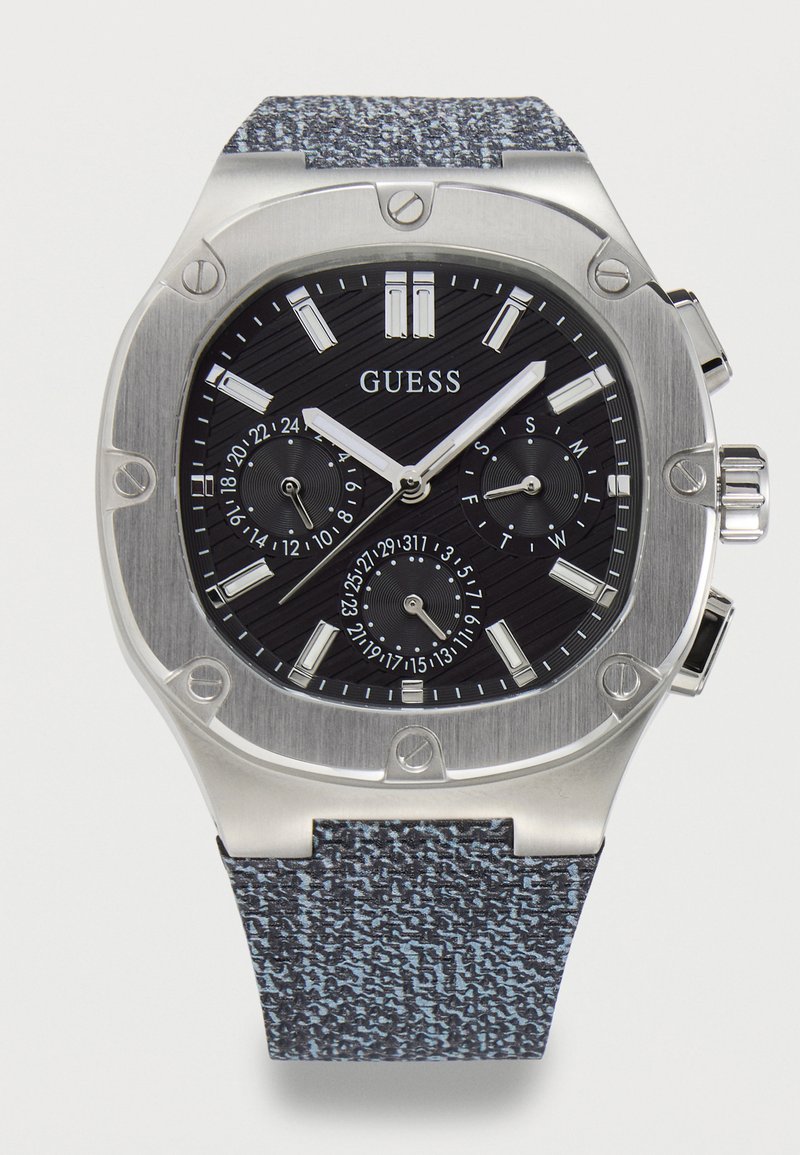 Montre-bracelet pour hommes Guess avec cadran multifonction noir, boîtier en acier inoxydable argenté et bracelet en tissu texturé bleu-gris.