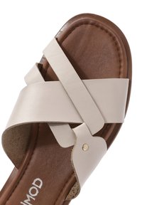 Sandale en cuir beige à enfiler avec des brides croisées, une semelle intérieure texturée marron et un petit accent doré près de la base. Semelle plate.
