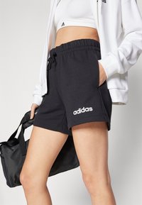 Svarte bomullsshorts med elastisk midje og snor, med hvit "adidas"-logo på venstre ben og sidelommer.