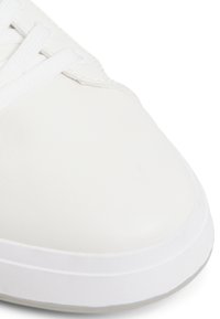Zapatilla de cuero blanco con superficie lisa, que presenta cordones blancos y puntera redonda. Suela blanca gruesa con una textura sutil en el borde.