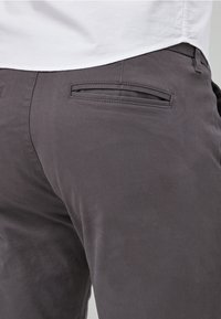 Tamno sivi hlače napravljene od glatkog materijala, s dekorativnom stražnjom džepom koji ima jedinstveni horizontalni detalj šivanja.