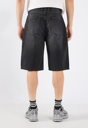 Czarne szorty dżinsowe o regularnym kroju, z tylnymi kieszeniami, prostym cięciem i podwiniętym dołem, w połączeniu z szarym obuwiem sportowym i w paski skarpetkami.