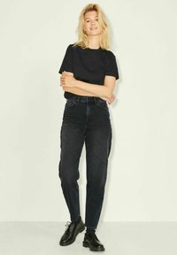Camiseta negra combinada con jeans de mezclilla oscuros de cintura alta. Los jeans tienen un diseño de pierna recta y se llevan con zapatos negros de cordones.