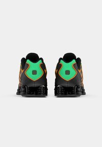 Čierne atletické topánky s zelenými a oranžovými akcentmi. Majú textúrovaný opätok, polstrovaný golier a vzorovanú podrážku pre lepšiu trakciu.