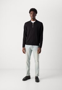 Black zip-up sweater, light blue jeans, and black shoes. Sweater has ribbed cuffs and hem; jeans are slightly fitted with a faded look.
