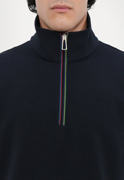 Sudadera de tejido suave de color azul marino con cremallera de media altura y alto cuello, que presenta una cremallera multicolor, diseñada para mayor comodidad y versatilidad.