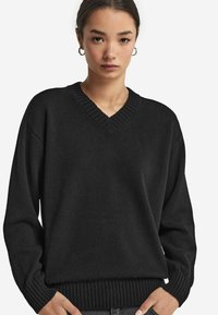 Czarny sweter z dzianiny z dekoltem w serek, ściągaczami na mankietach i u dołu. Luźny krój o miękkiej fakturze, zaprojektowany z myślą o komforcie i ciepłocie.