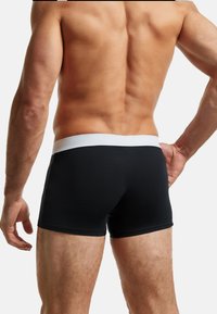 Biancheria intima hipster nera con una cintura bianca, realizzata in un materiale liscio ed elastico. Presenta un design aderente e cuciture minime.