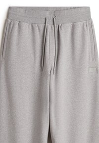 Lichtgrijze sportbroek met een trekkoord in de taille, zijzakken en een klein rubberen logo-patch op het linkergedeelte. Zachte jersey stoftextuur.