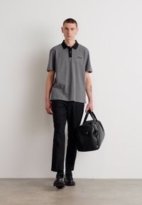 Šedé polo tričko s čiernym golierom, krátkymi rukávmi a decentným logom. Čierne nohavice a lesklá čierna športová taška dopĺňajú tento outfit.