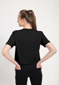 Czarny krótki rękaw t-shirt z okrągłym dekoltem, wykonany z gładkiego materiału. Nosi go osoba z rękami na biodrach, prezentujący prosty, jednolity wzór.