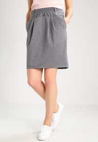 Jupe grise plissée en tissu texturé, dotée d'une ceinture ajustée et de poches latérales, associée à des chaussures blanches sans lacets.