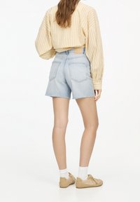 Light beige oversized ribbed sweater, light blue denim shorts with frayed edges, and tan shoes with white socks.