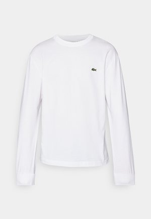 Tricou alb cu mânecă lungă fabricat din bumbac. Are un guler rotund cu dungi și un mic logo brodat verde pe piept. Design simplu.