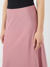 Jupe rose avec une texture lisse, dotée d'une taille haute. Gros plan montrant le tombé du tissu et la position des mains contre la jupe.