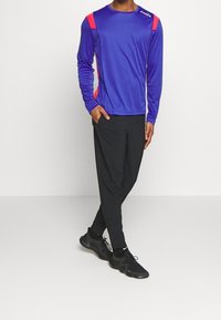 Blå långärmad träningsskjorta med röda detaljer, kombinerad med svarta byxor och svarta sneakers, med en bekväm passform och slät textur.