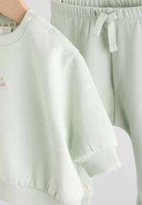 Sweat-shirt en coton vert clair avec poignets côtelés et un petit détail brodé, assorti à un pantalon avec une taille élastique.