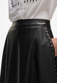 Fekete bőrszoknya sima textúrával, magas derékkal és oldalsó gomb részletekkel. Fém címke található a derékon.