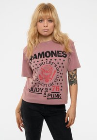 Short-sleeve, faded pink graphic t-shirt featuring black text, star accents, and an eagle design. Worn with dark jeans.