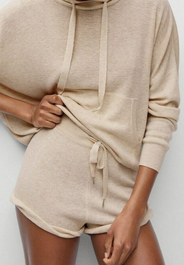 Conjunto de ropa cómoda de punto beige que incluye una sudadera holgada con capucha, cordones y un bolsillo frontal, combinada con pantalones cortos a juego ajustados a la cintura.