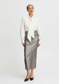 Blouse blanche avec un détail de cravate et des manches longues, associée à une jupe crayon métallique argentée ajustée et des escarpins noirs à bout pointu.