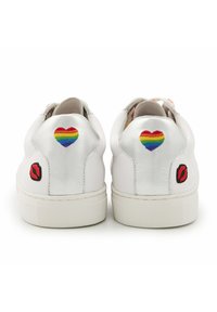 Baskets blanches avec des accents métalliques, présentant un cœur arc-en-ciel et une broderie de lèvres rouges à l'arrière. Semelle en caoutchouc, design à bout rond.