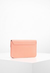 Brzoskwiniowa kopertówka ze skóry o gładkiej fakturze, prostokątnym kształcie i klapie zamykającej. Charakteryzuje się minimalnym przeszyciem i brakiem metalowych zdobień.