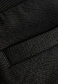 Črna tkanina z mehko, pleteno teksturo. Ponaša se z rebrasto pasom in gladko površino, ki prikazuje preprosto, enobarvno obliko.