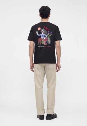 Homme de dos portant un t-shirt noir avec une illustration colorée d'une personne, des fleurs, une bouteille et un ballon de basket dans le dos.